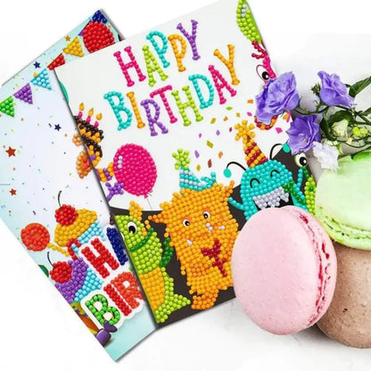 Diamond painting verjaardagskaart met kleurrijke monsters en de tekst 'Happy Birthday', omringd door macarons en bloemen