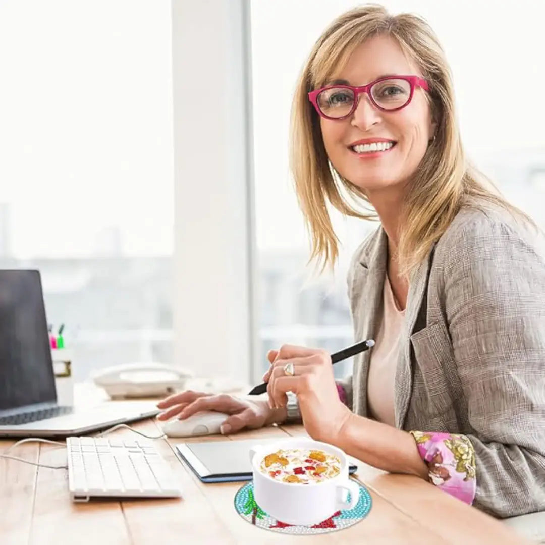 Vrouw met bril werkt aan bureau met kop koffie op een ronde diamond painting onderzetter.