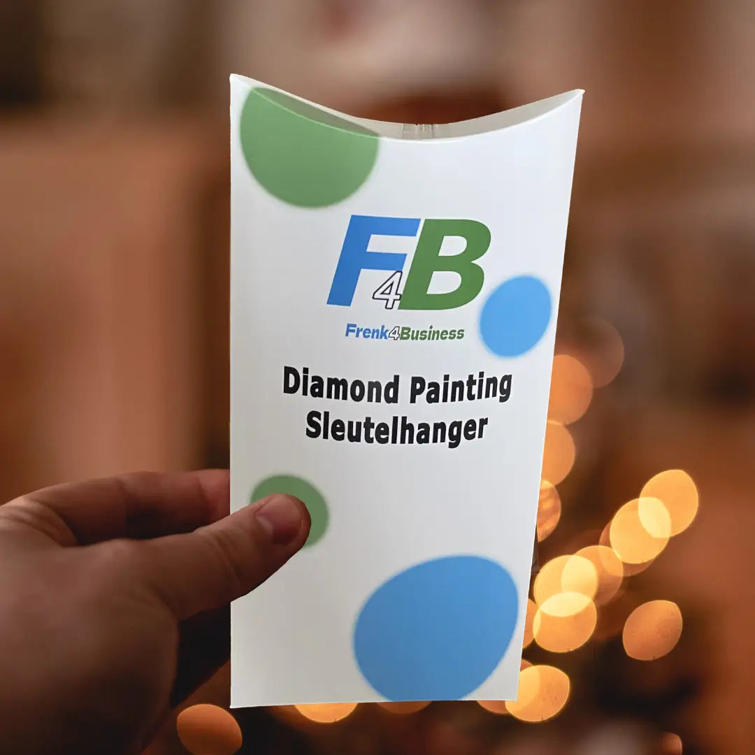 Hand die een verpakking met "Diamond Painting Sleutelhanger" van Frenk4Business vasthoudt, met sfeerverlichting op de achtergrond.