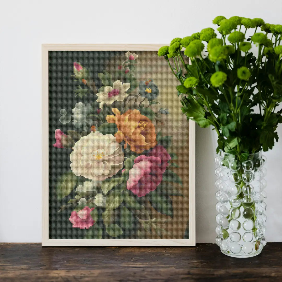 Ingelijste diamond painting van een klassiek bloemenboeket op een houten tafel naast een vaas met groene chrysanten