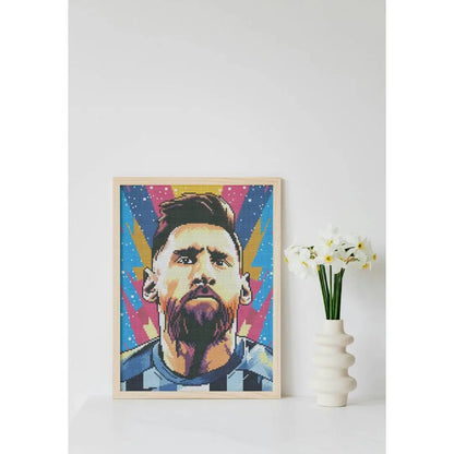 Ingelijste diamond painting van een voetballer met felle kleuren, geplaatst op een tafel naast een witte vaas met bloemen.